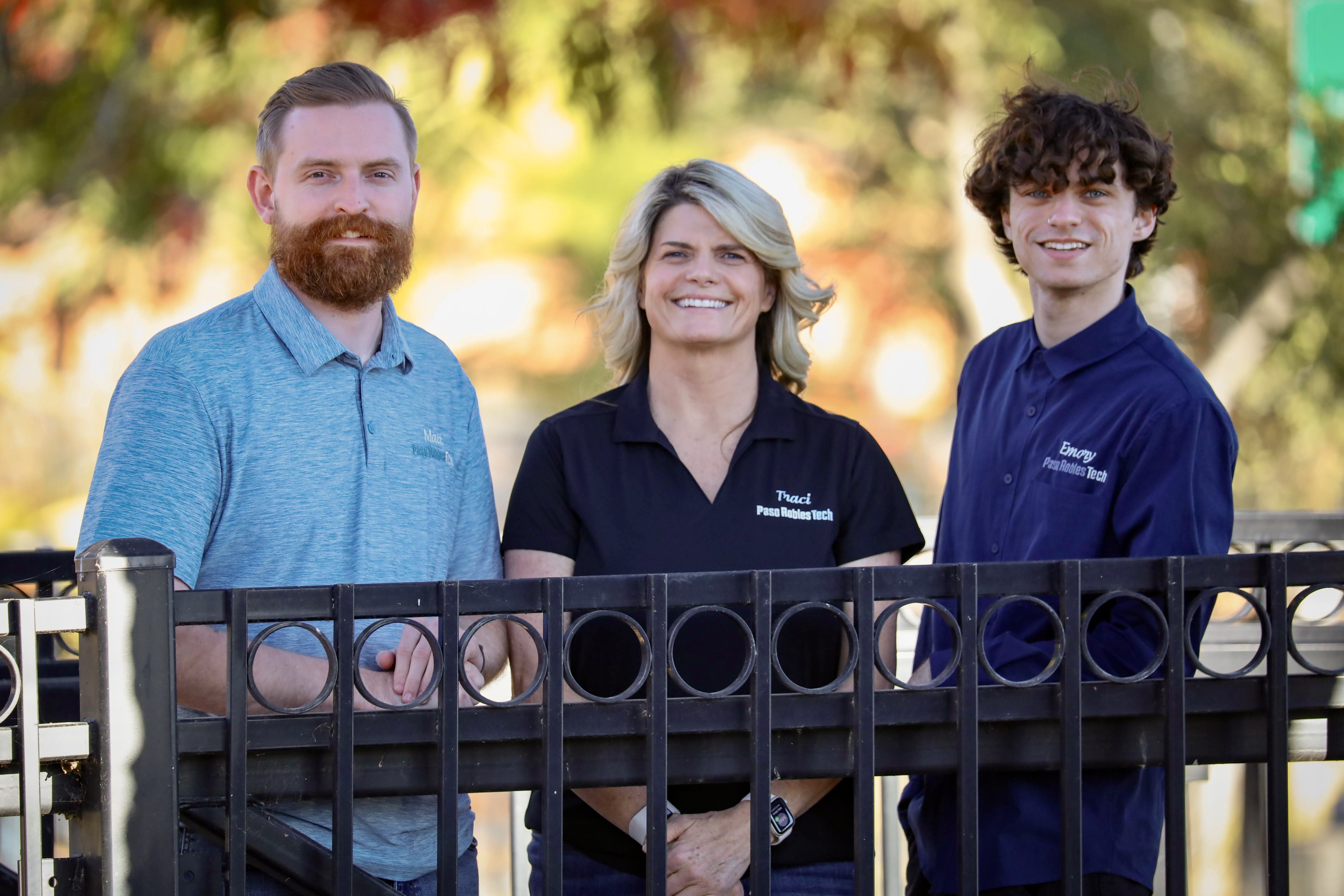 Matt, Traci, and Emory of Paso Robles Tech standing together outdoors behind an iron railing on a tree-lined street